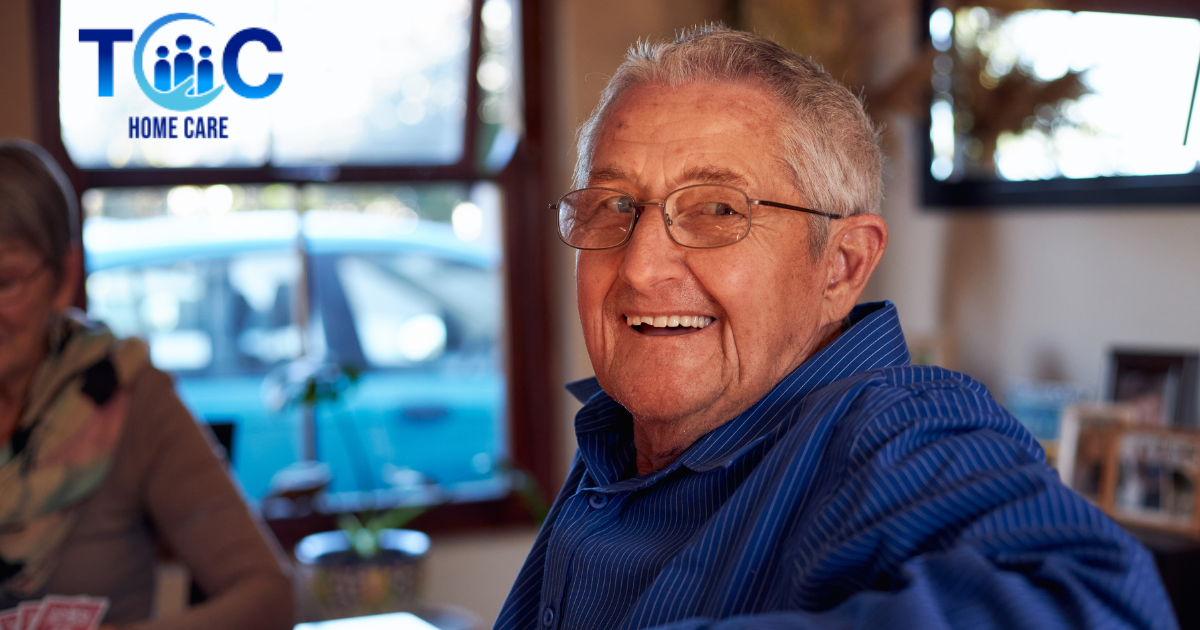 Smiling senior man who is happy as a result of successful long-distance caregiving is sitting at a table and looking over his shoulder.