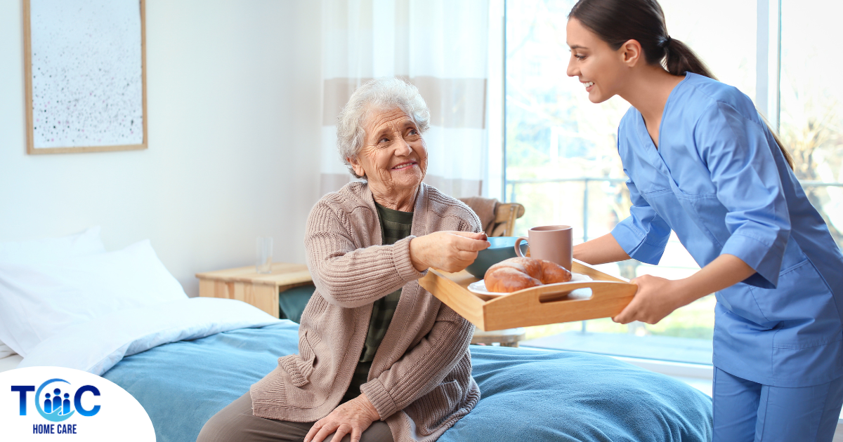 A professional caregiver smiles and provides food to an older adult in her care, representing the compassionate care needed for those with dementia.