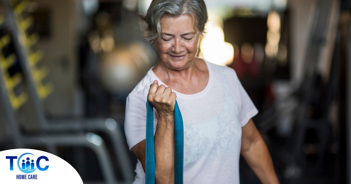 An older woman uses a resistance band to exercise, representing how staying active can help older adults keep their blood pressure in a healthy range.