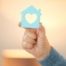 A hand holds up a cutout of a home with a heart in it, representing the home care industry.