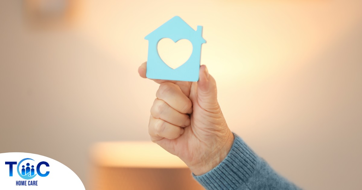 A hand holds up a cutout of a home with a heart in it, representing the home care industry.