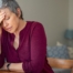 A woman holds her head in her hand, representing the stress that new family caregivers go through.