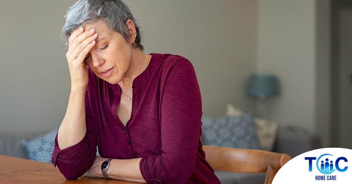 A woman holds her head in her hand, representing the stress that new family caregivers go through.