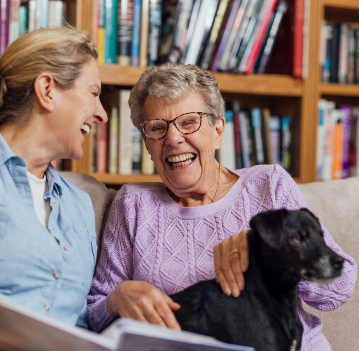 Companionship Care in Pasadena (2) Senior woman smiling and spending time with a caregiver during Companionship Care in Pasadena at home with a pet dog nearby.