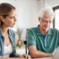 Adult daughter and senior father talking at a kitchen table while comparing home care vs assisted living